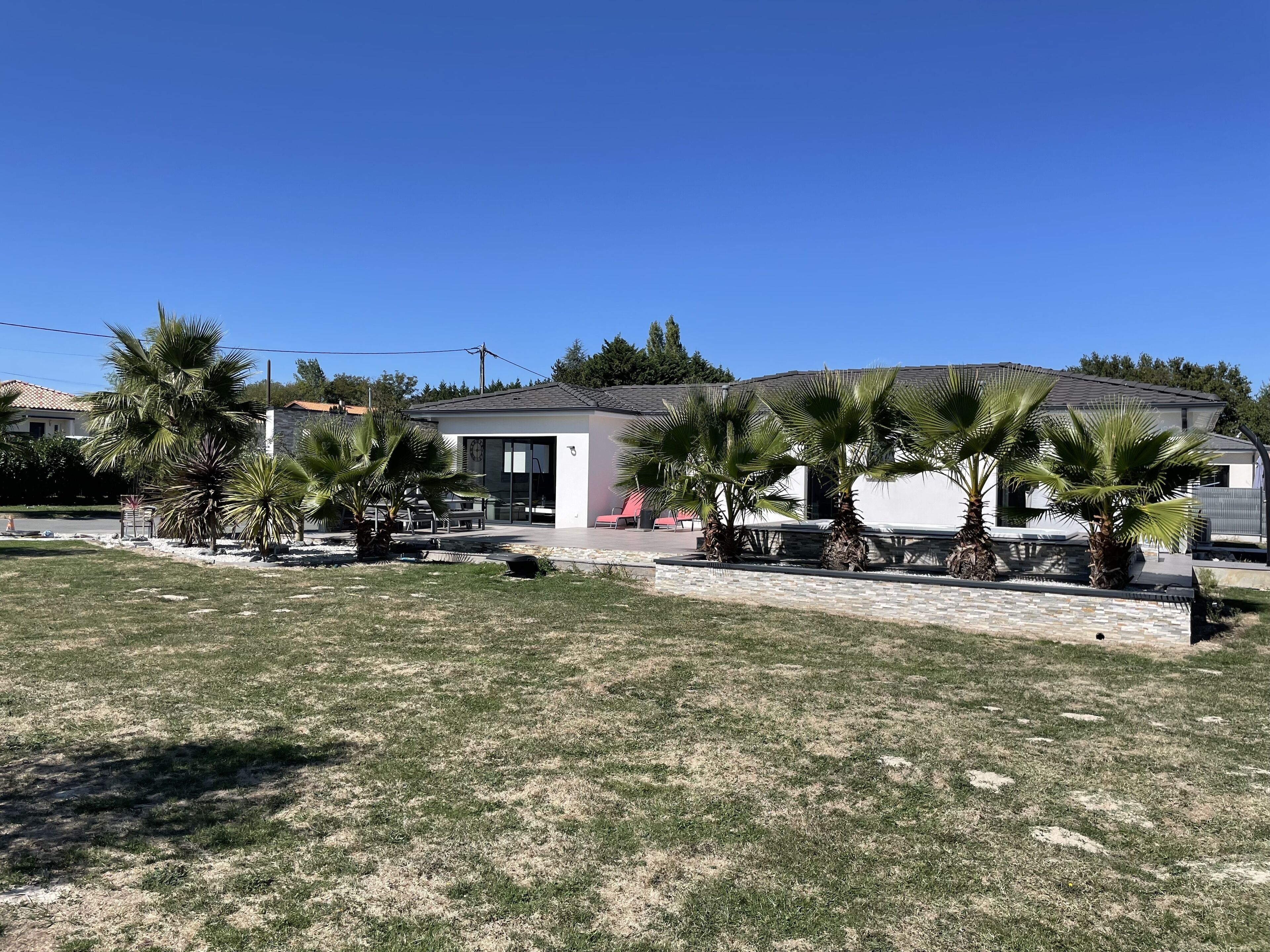A modern house with a patio area, surrounded by palm trees and a well-maintained lawn.