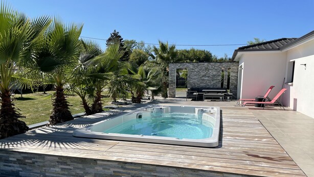 Tinaja rectangular sobre una terraza de madera con escalones de piedra, rodeada de palmeras y un muro de piedra.