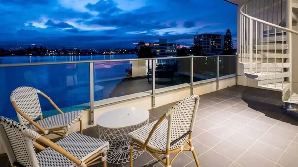 Un balcón con piscina, mobiliario de mimbre y vista a la ciudad al atardecer.