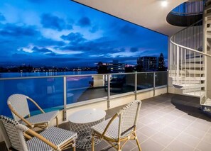 Un balcon avec une piscine, des meubles en osier et une vue sur la ville au crépuscule.