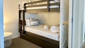 Una cama litera con cabecera, una mesita de noche y una pequeña mesa redonda con estructura de alambre.