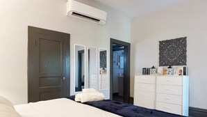 Ein Schlafzimmer mit Bett, Kleiderschrank, Schminktisch, Klimaanlage und einer Tür zu einem anderen Raum.