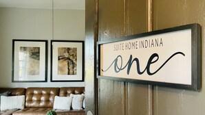 Ein Wohnzimmer mit braunem Ledersofa, zwei gerahmten abstrakten Gemälden und einem Schild mit der Aufschrift 'SUITE HOME INDIANA one'.
