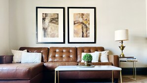 Ein Wohnzimmer mit einem braunen Ledersofa, einem weißen Couchtisch und zwei gerahmten abstrakten Bildern an der Wand.
