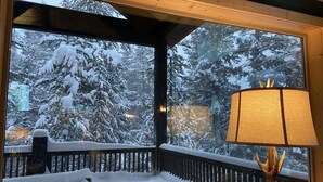Ein Zimmer mit großem Fenster mit Blick auf eine schneebedeckte Terrasse und Bäume.
