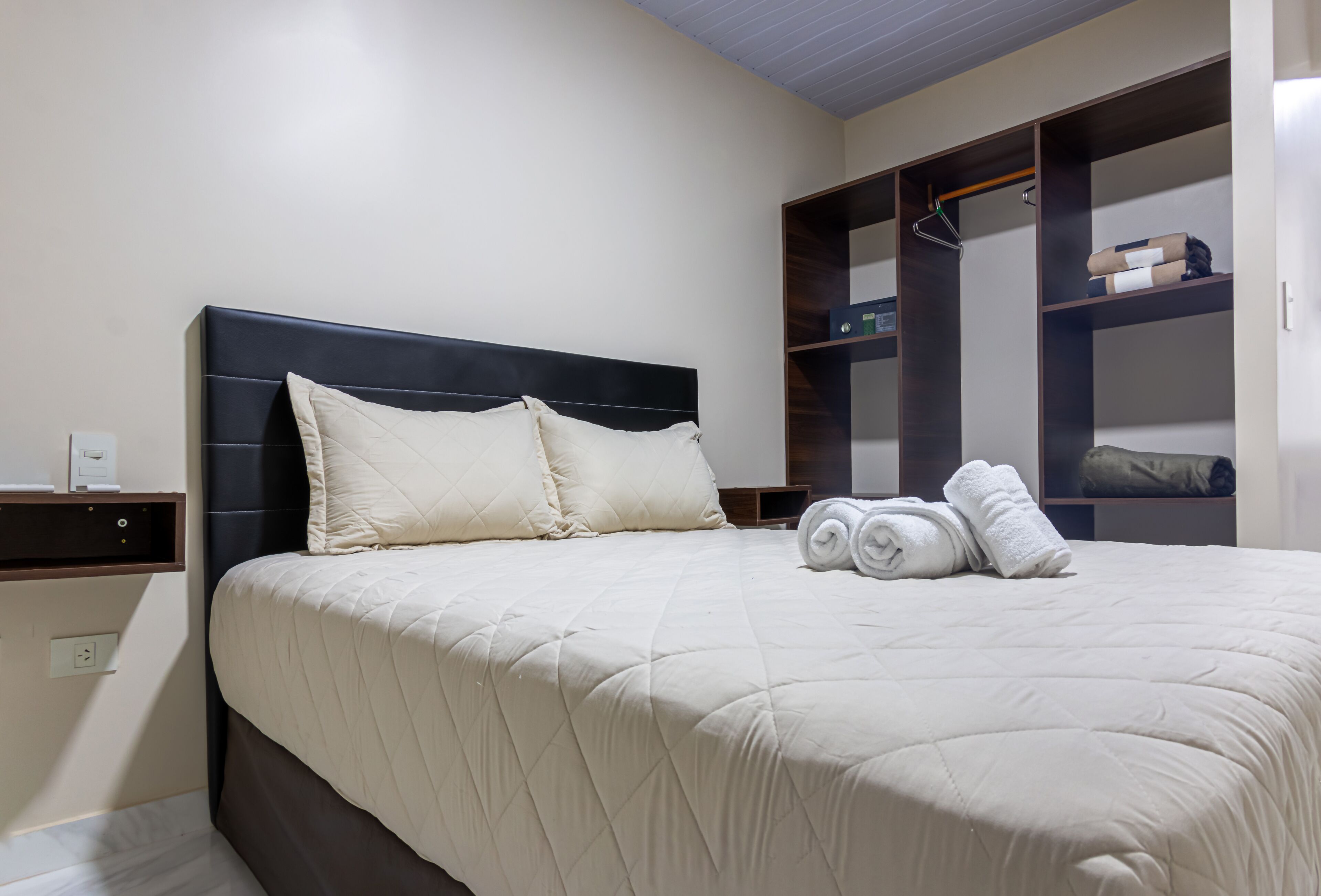 A neatly made bed with a quilted headboard, a bedside table with a lamp, and a built-in wardrobe with shelves.