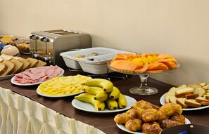 Ein reichhaltiges Buffet mit verschiedenen Speisen, darunter Brot, Schinken, Eier, Bananen und Gebäck.