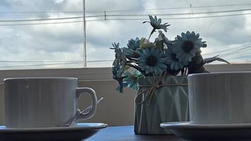 Taula amb dues tasses i platets, un ram de flors artificials i vista del cel amb núvols.