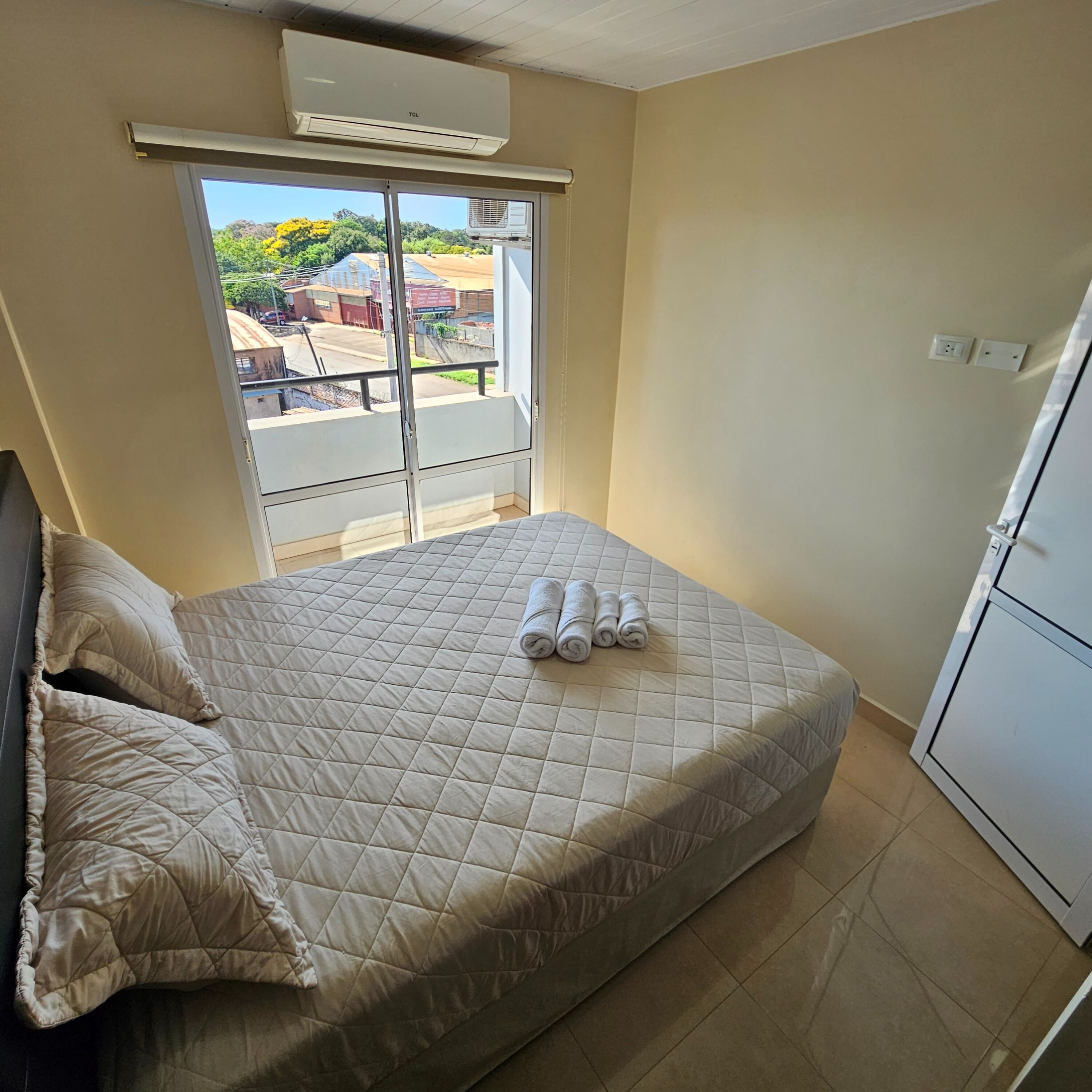 Ein Schlafzimmer mit Bett, Kissen, einem Fenster mit Blick, einer Klimaanlage und einem weißen Gerät.