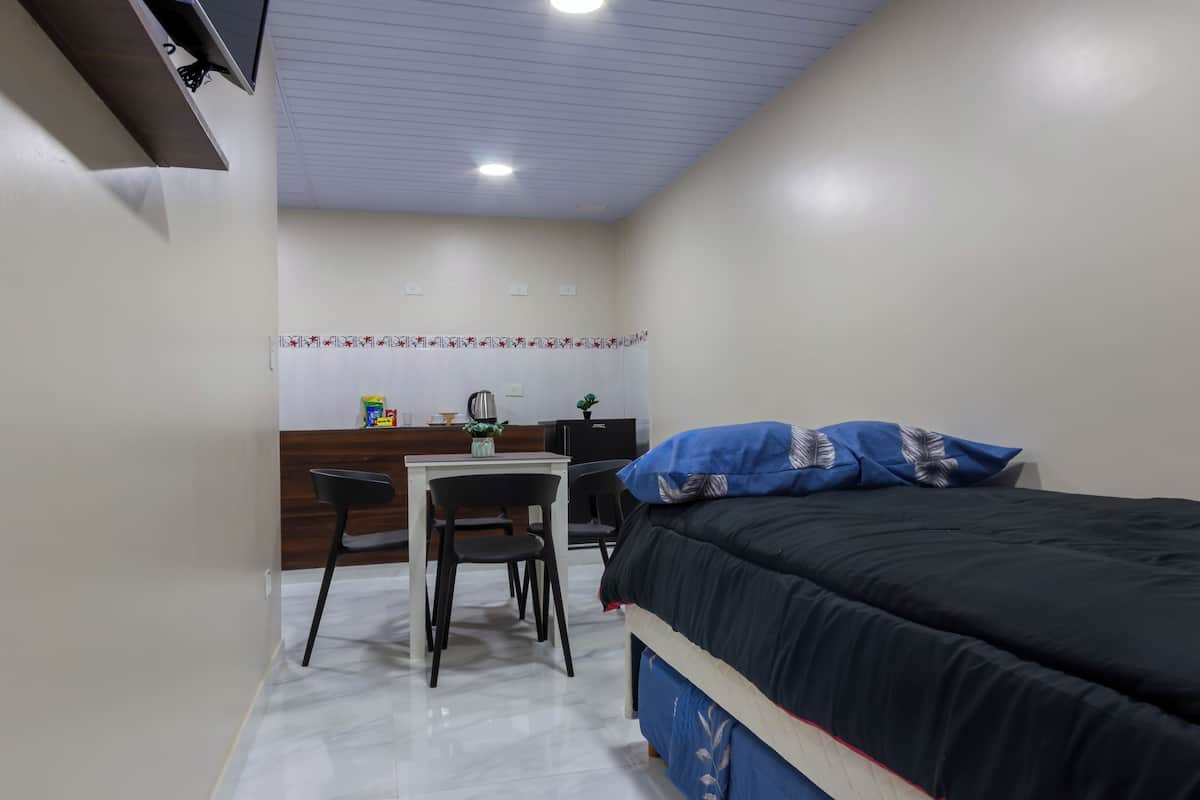 Ein Schlafzimmer mit Bett, Schreibtisch, Stuhl und einer kleinen Küchenzeile.