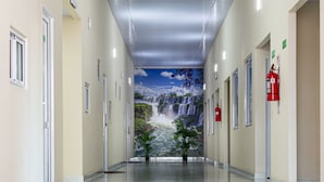 Een lange, goed verlichte gang met een marmeren vloer, deuren aan beide zijden en een muurschildering van een waterval op de verre wand.