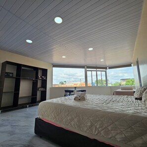 Ein Schlafzimmer mit einem großen Bett, einem Kleiderschrank und einem Schreibtisch. Fenster bieten einen Blick nach draußen.