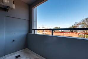 Ein Zimmer mit großem Fenster, einem Balkon mit Metallgeländer und Blick auf eine Baustelle mit rotem Zaun.