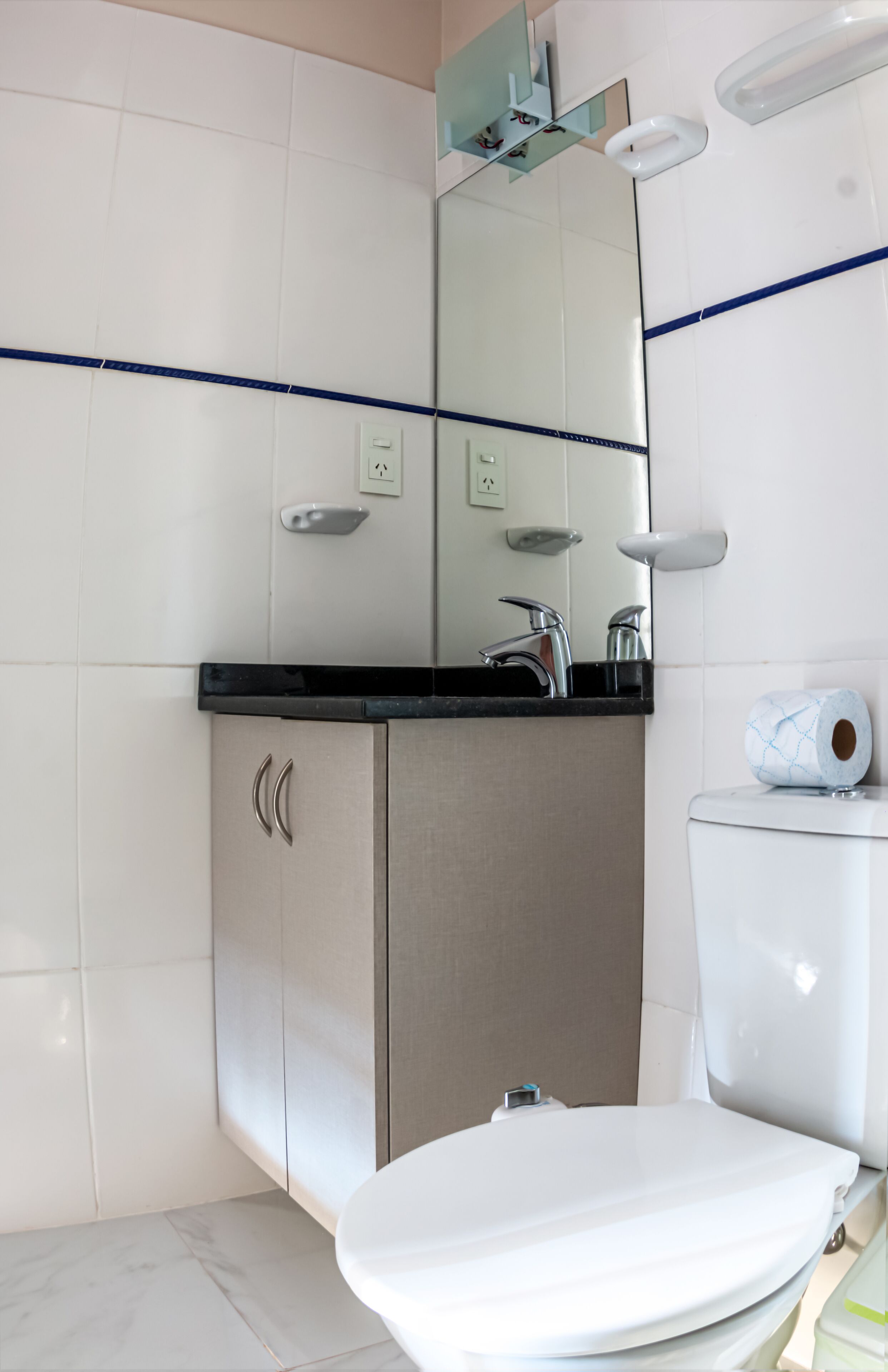A modern bathroom with a white toilet, a sink with a black countertop, and a mirror above the sink.