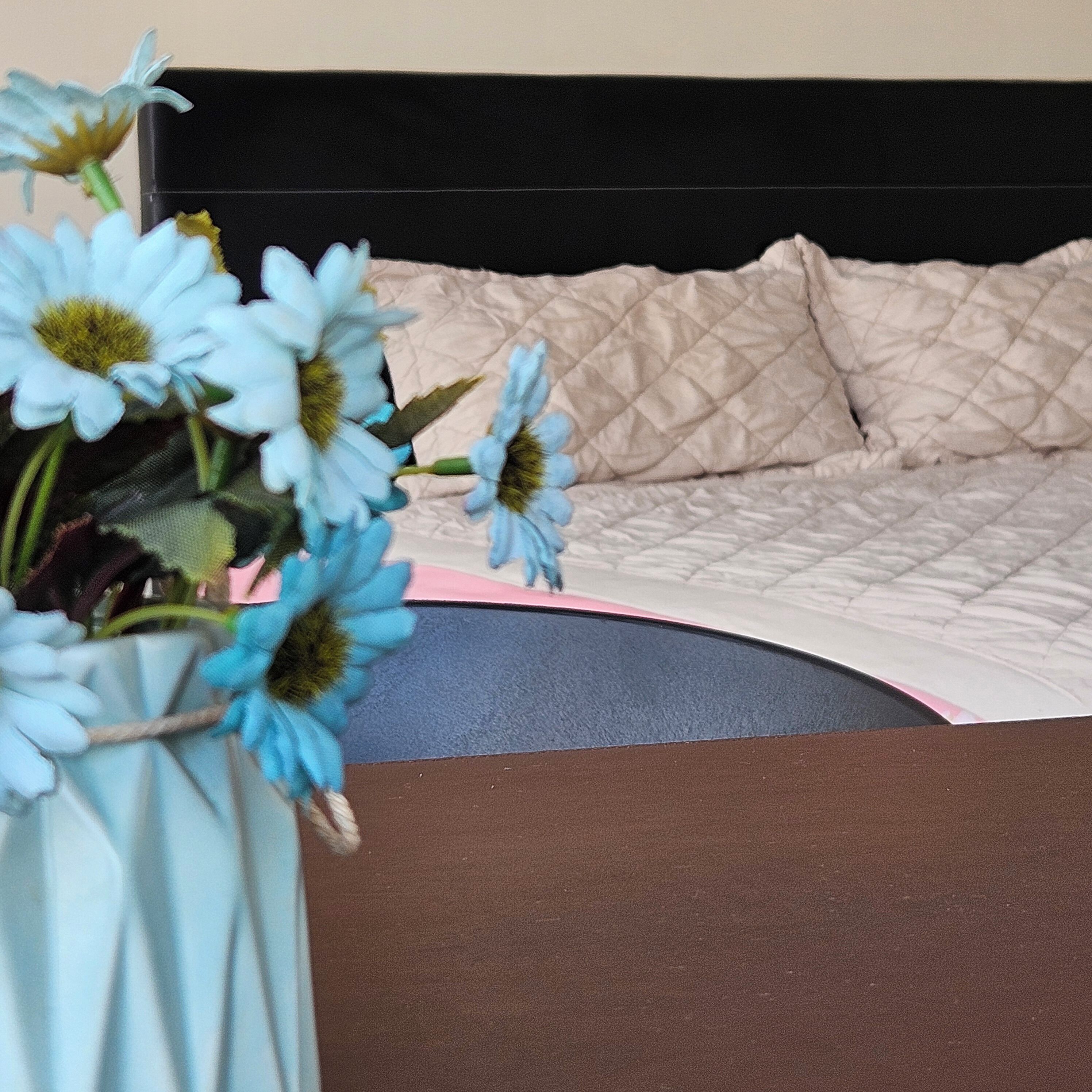Ein Bett mit einer gesteppten Kopfteil und einer Blumenvase auf einem Nachttisch.