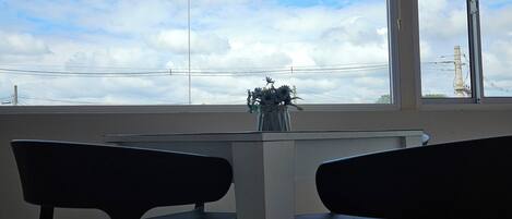 Un comedor con una mesa y sillas, vista al cielo a través de una ventana y un florero con flores sobre la mesa.