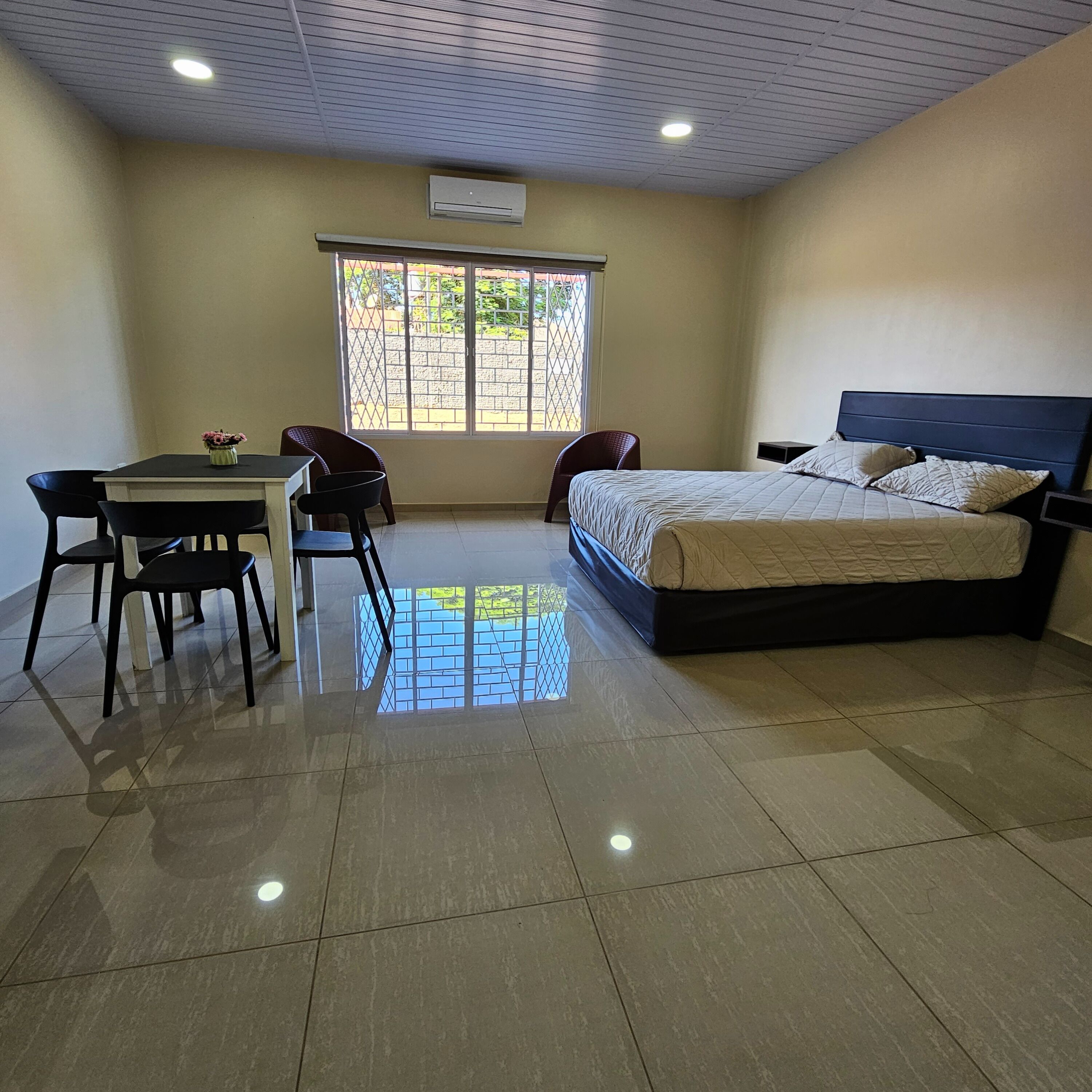Un dormitorio con cama, una mesa con sillas, un ventanal y un equipo de aire acondicionado.