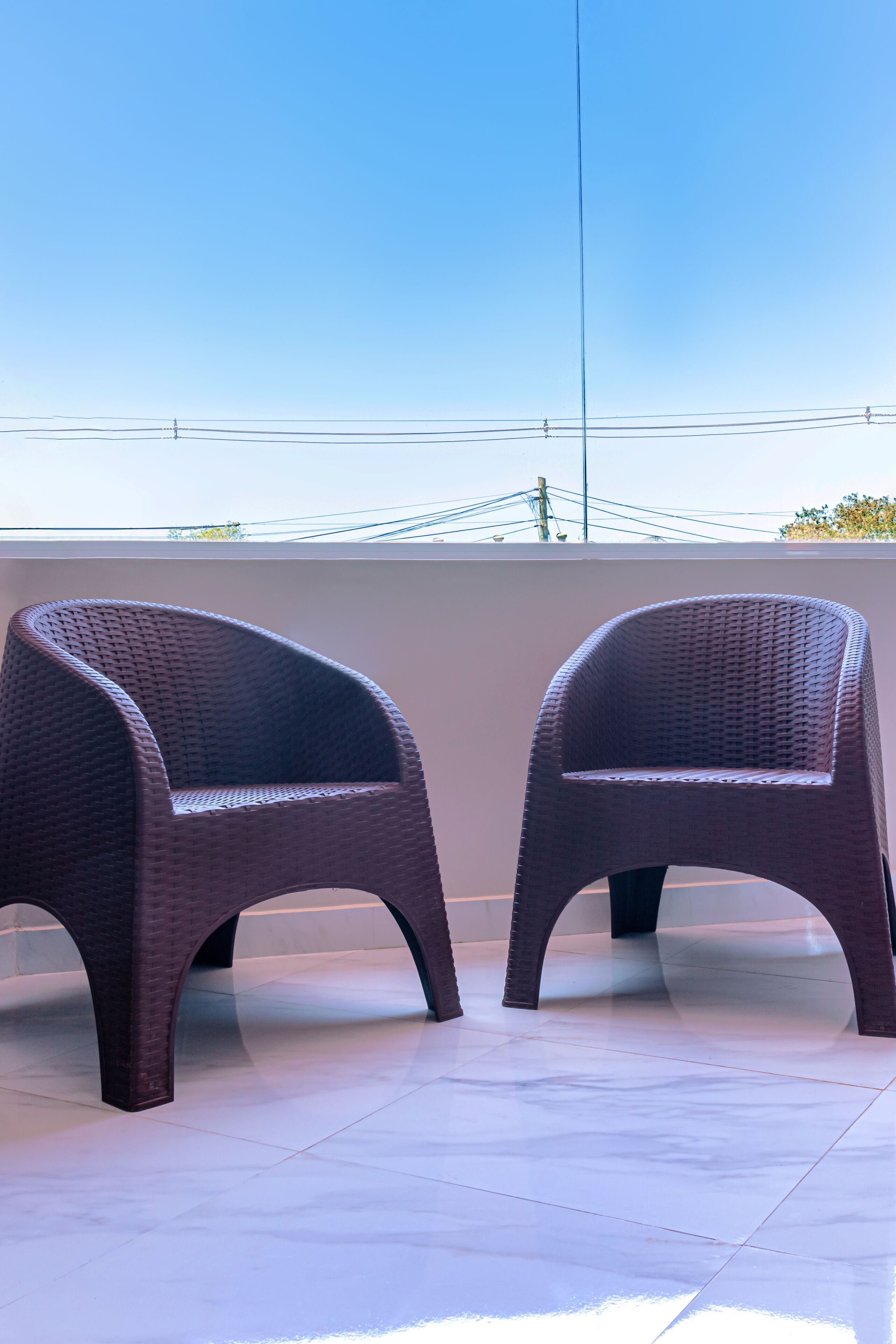 Two wicker chairs on a tiled patio with a clear sky in the background.