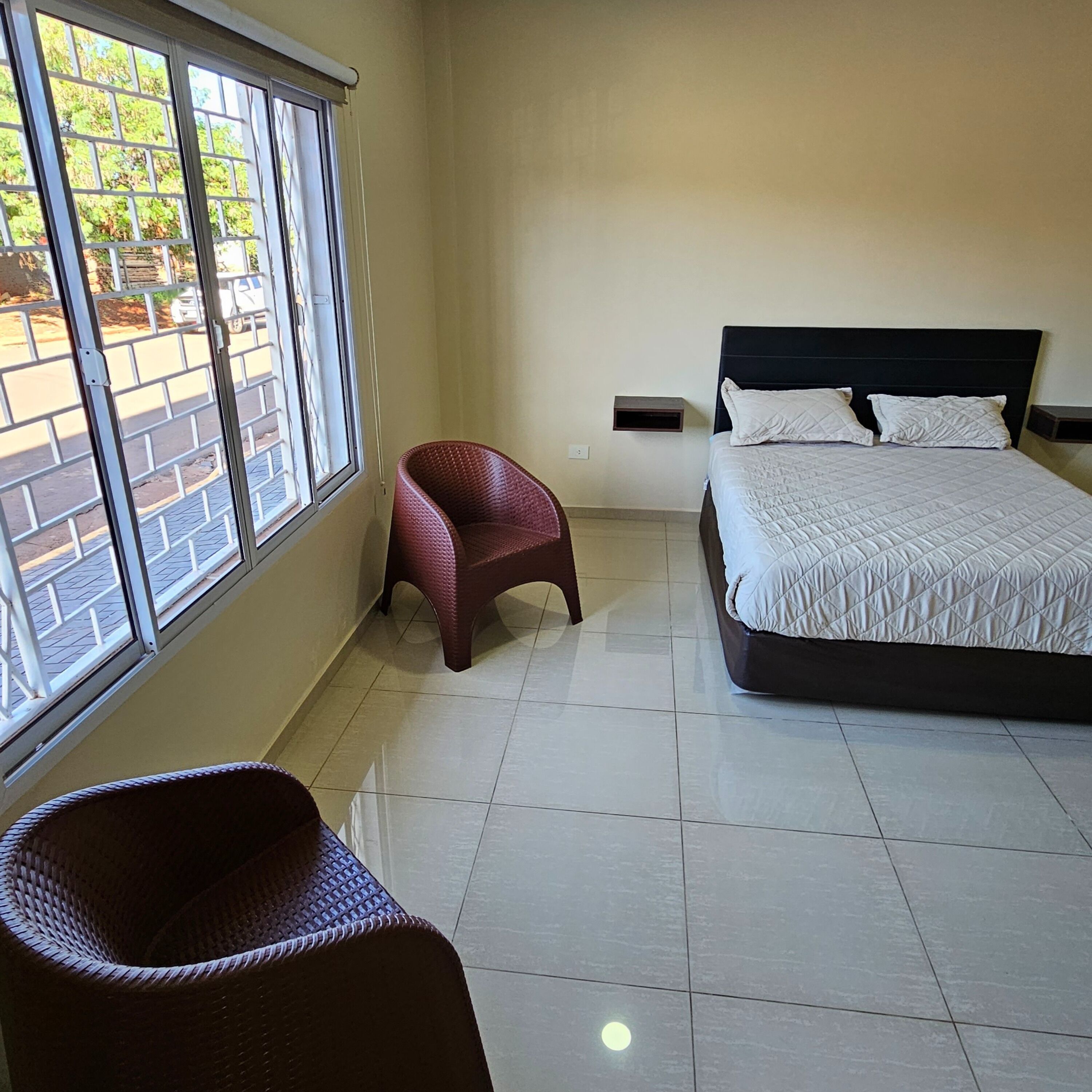A bedroom with a bed, a chair, a window, and a tiled floor.