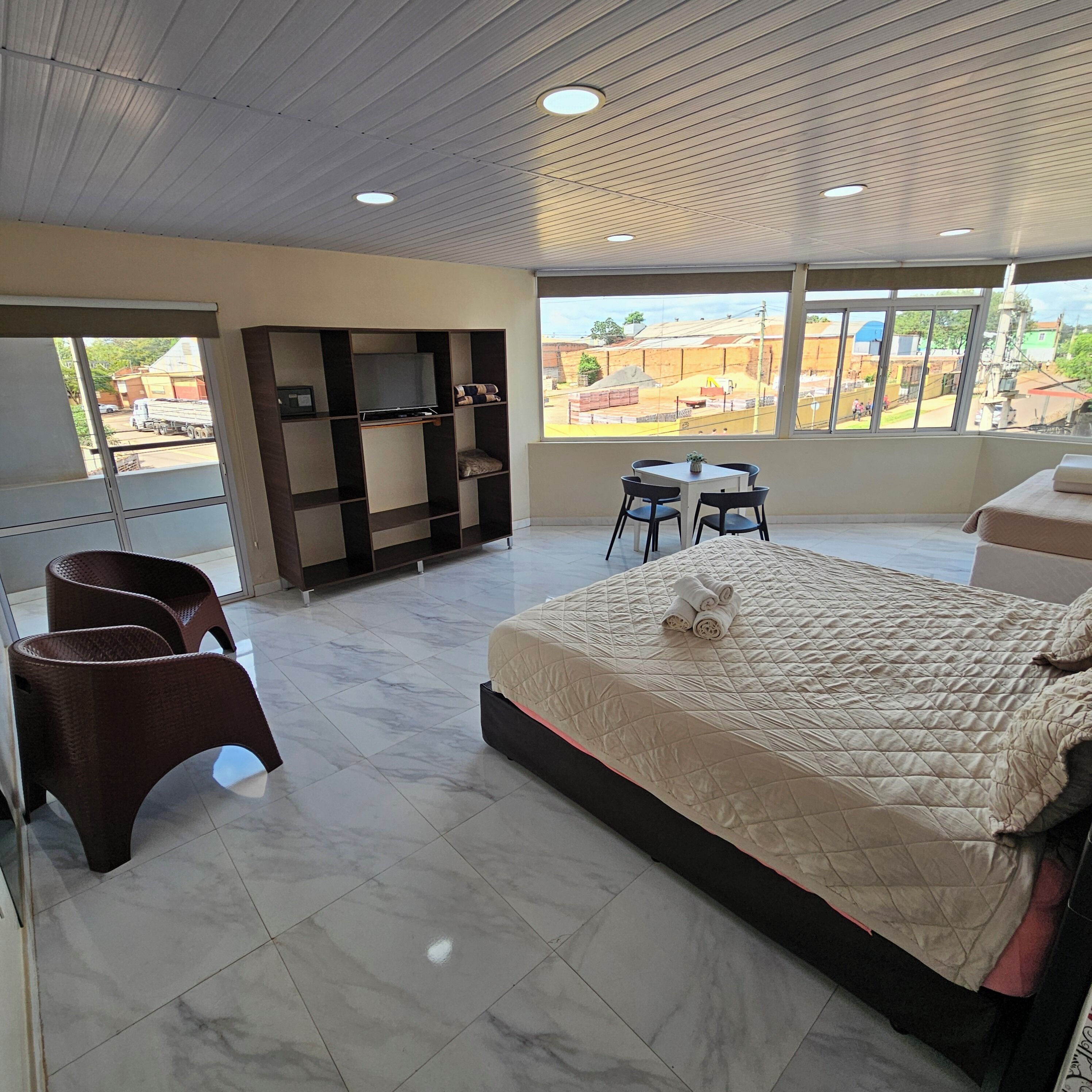 Una camera d'albergo moderna con un letto grande, una zona salotto con poltrone, una TV su un mobile e vista sull'esterno.