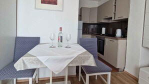 Uma área de refeições com uma mesa, duas cadeiras, um quadro emoldurado e uma cozinha ao fundo.