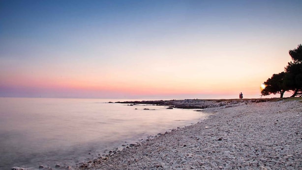 Uma praia de seixos com um mar calmo e um céu ao pôr do sol.