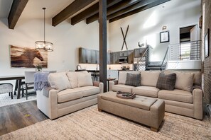 A spacious living area with two sofas, a coffee table, and a dining table. There is a staircase leading to an upper level.