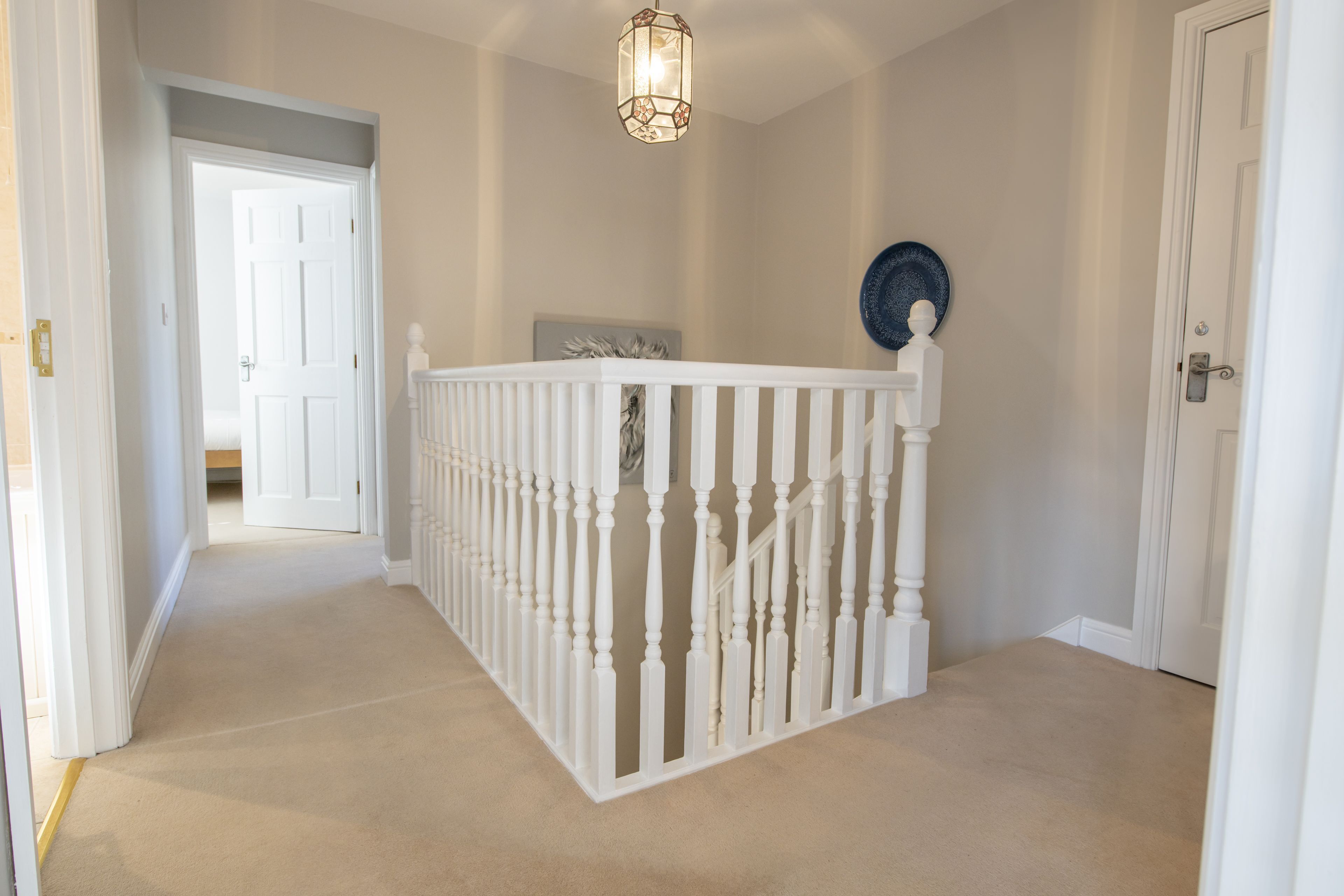 A hallway with a white railing, beige carpet, and a decorative light fixture.