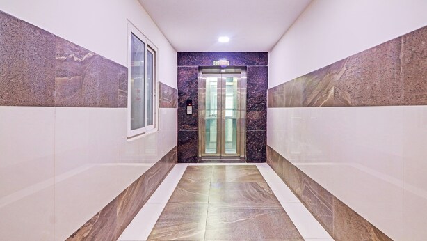 A hallway with marble flooring and walls, leading to an elevator with a 'No Smoking' sign above it. - Itsy Hotels Aura Stays (Hyderabad)