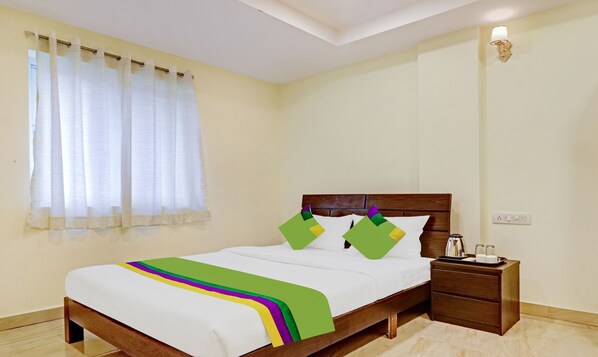 A neatly made bed with a white and green bedspread, a wooden headboard, and a nightstand with a tray of items. - Itsy Hotels Aura Stays (Hyderabad)