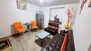 Un espacio habitable compacto con un sofá, dos sillas, una mesita, un refrigerador y un jarrón decorativo.