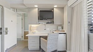 A compact kitchen with a built-in TV, a small fridge, and a wicker chair. - Oceanside Cozy, Clean, Casual Suite - steps to beach and amenities!    (Kihei)