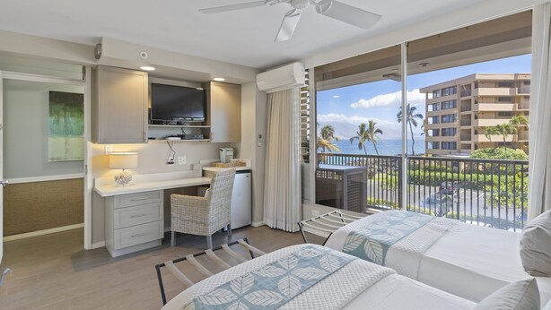 A hotel room with a balcony, a desk, a chair, a bed, and a ceiling fan. - Oceanside Cozy, Clean, Casual Suite - steps to beach and amenities!    (Kihei)