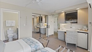A compact hotel room with a bed, a small kitchenette, a bathroom, and a ceiling fan. - Oceanside Cozy, Clean, Casual Suite - steps to beach and amenities!    (Kihei)