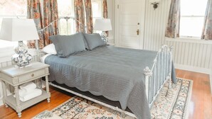 A neatly arranged bedroom with a bed, two bedside tables, a nightstand, a lamp, and a patterned rug. - The Cottage: One bedroom w/mini fridge & private bath. (Medford)