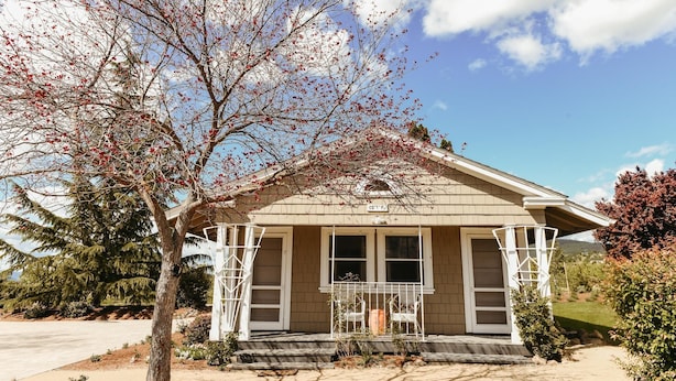 A single-story house with a porch, a small garden, and a clear sky. - The Cottage: One bedroom w/mini fridge & private bath. (Medford)
