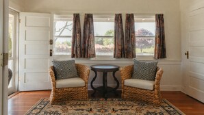 A room with two wicker chairs, a small round table, and a patterned rug. - The Cottage: One bedroom w/mini fridge & private bath. (Medford)