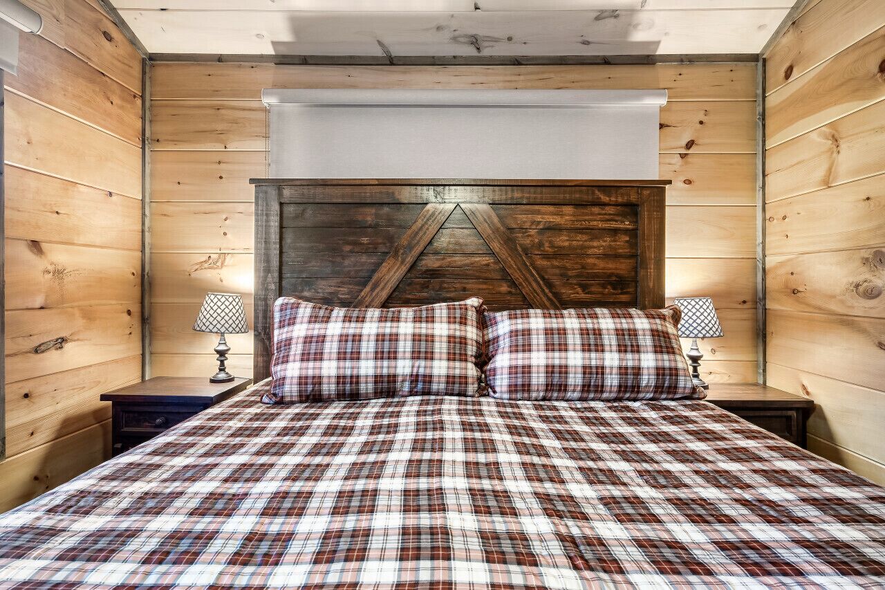 Een kamer met houten lambrisering, een bed, twee nachtkastjes en een raam met een witte jaloezie.