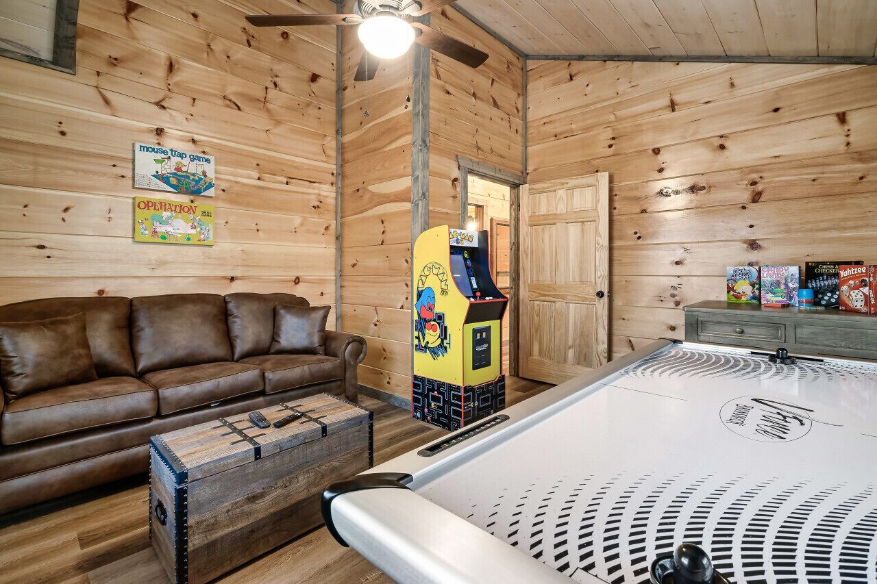 Una habitación acogedora con un sofá de cuero marrón, una mesa de billar y una máquina de garrapatas.
