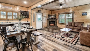 A cozy cabin interior with a dining area, a fireplace, and a living room furnished with a sofa and a coffee table. - Modern 4BR Cabin ★ Amazing Location Near Dollywood ★ Grotto Hot Tub ★ Game Room (Sevierville)