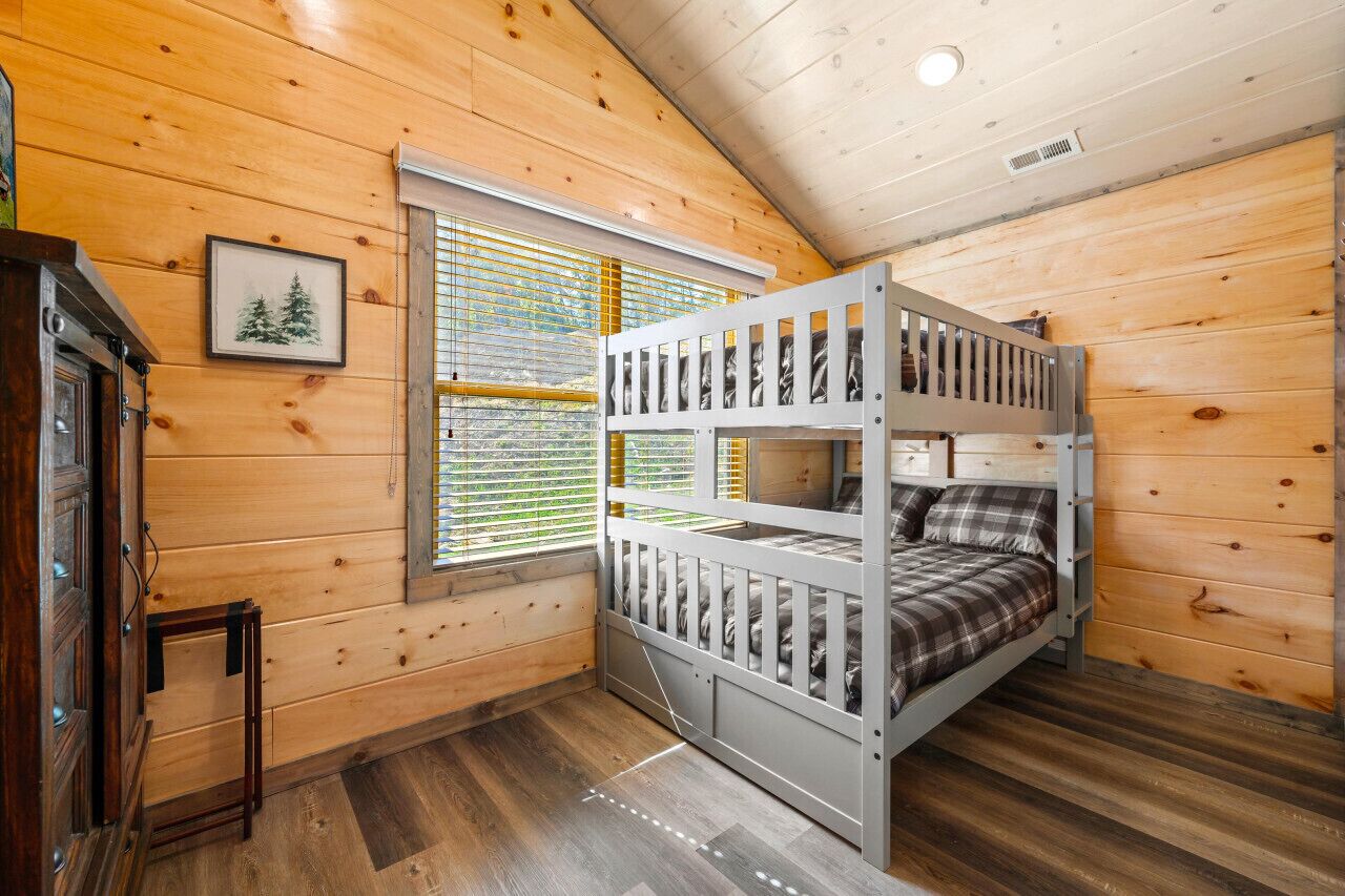 A bunk bed room with wooden walls and a window with blinds.