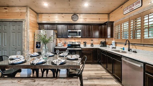 A wooden interior with a dining table set for six, a kitchen with dark cabinets, a microwave, and a coffee station. - Modern 4BR Cabin ★ Amazing Location Near Dollywood ★ Grotto Hot Tub ★ Game Room (Sevierville)