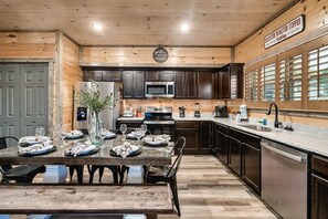 A wooden interior with a dining table set for six, a kitchen with dark cabinets, a microwave, and a coffee station. - Modern 4BR Cabin ★ Amazing Location Near Dollywood ★ Grotto Hot Tub ★ Game Room (Sevierville)