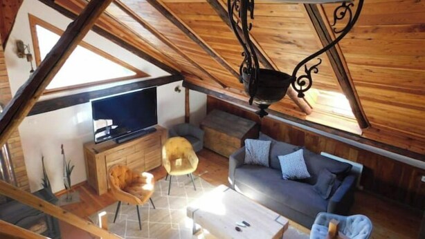 Ein gemütliches Dachzimmer mit Holzbalkendecke, einem Fernseher, einem Sofa und einem Esstisch.