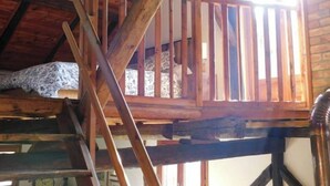 Ein Schlafzimmer im Spitzboden mit Holzbalken, einer Holzreling und einem Fenster für natürliches Licht.