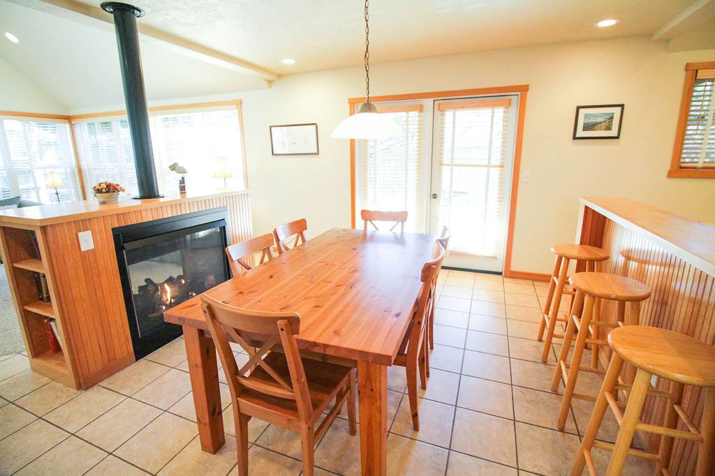 A dining area with a wooden table and chairs, a built-in stove, and a view of the outside through a glass door.