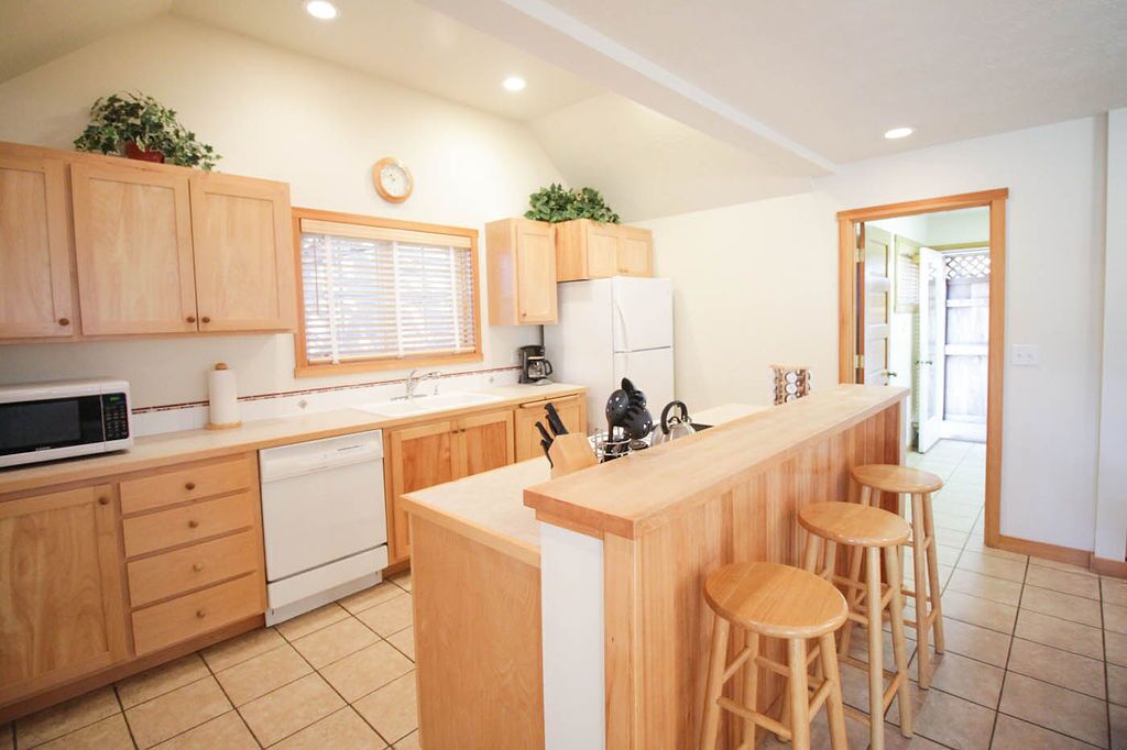 A modern kitchen with wooden cabinets, a microwave, a dishwasher, a sink, and a bar area with stools.