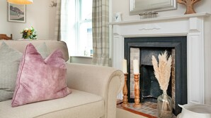 A living room with a beige sofa, a fireplace, and a window with curtains. - 2 bedroom accommodation in Malborough (Malborough)
