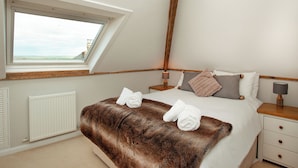 A bedroom with a sloped ceiling, a large window, a bed with a fur throw, and a nightstand with a lamp. - 2 bedroom accommodation in Malborough (Malborough)