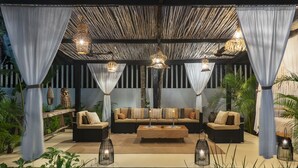 Un espace extérieur accueillant, doté d’un toit de chaume, de canapés confortables et de lanternes suspendues.